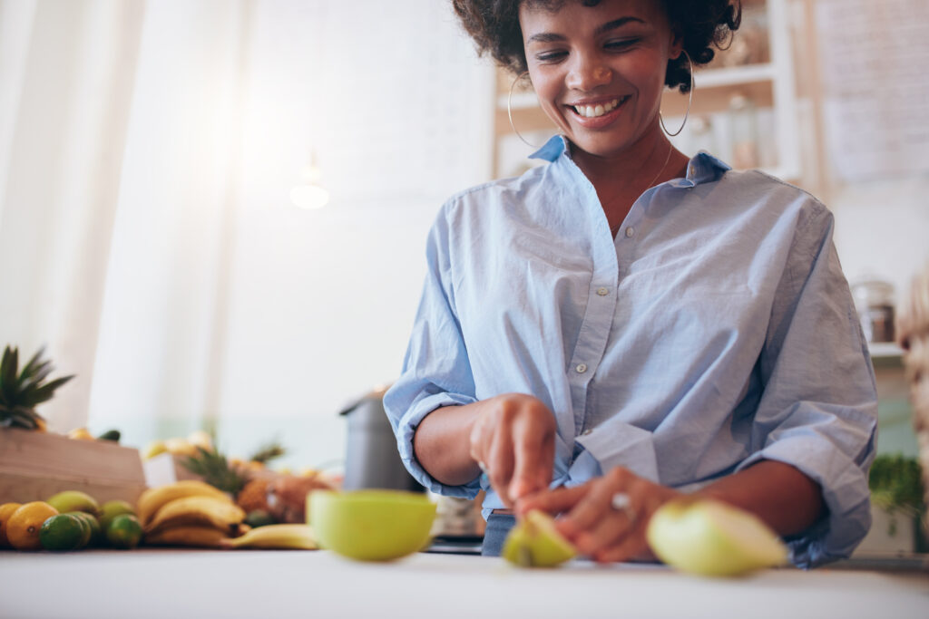woman smiling cutting an apple with other fresh produce around her. 
photo by adobe stock 