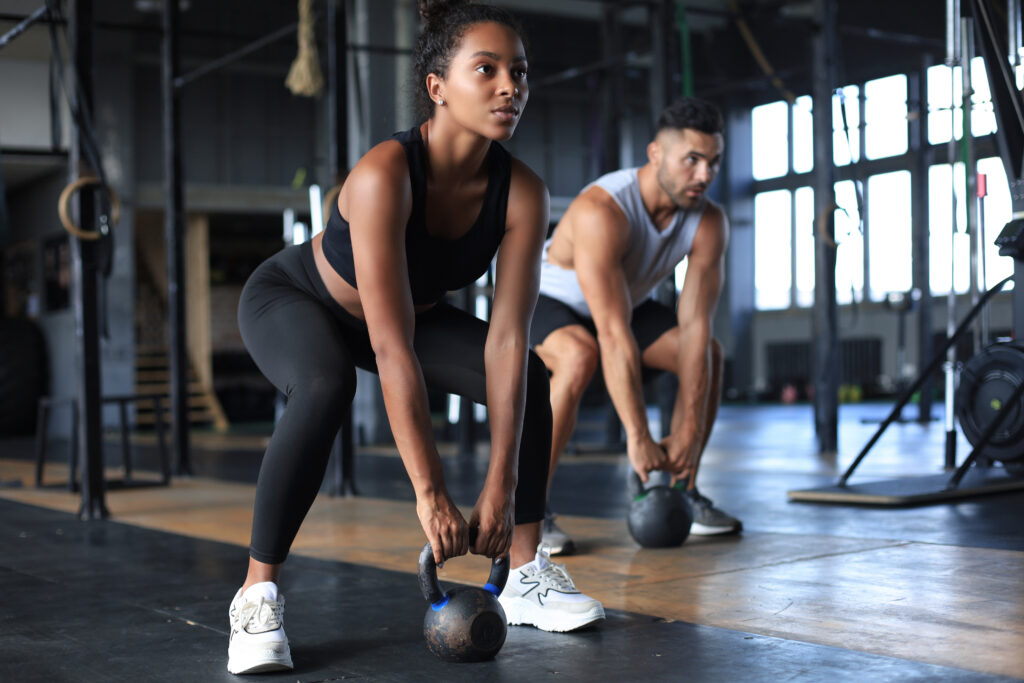 Fit and muscular couple focused on lifting a dumbbell during an exercise class in a gym By ty adobe stock