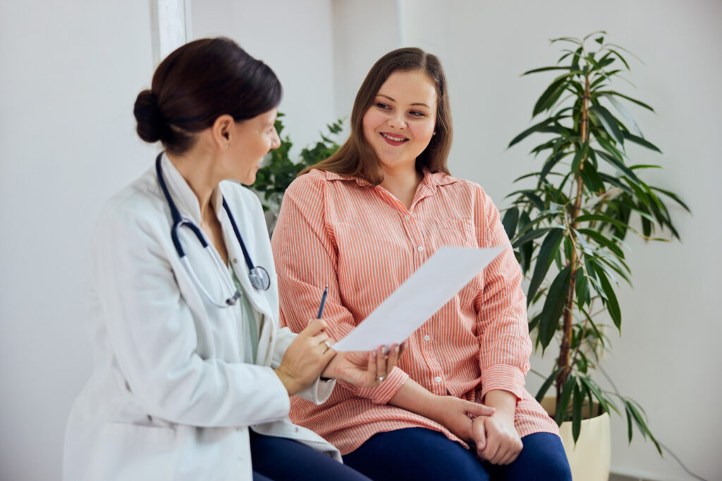 A satisfied female nutritionist holding a paper with weight loss progress and smiling with an overweight female patient. By bnenin adobe stock